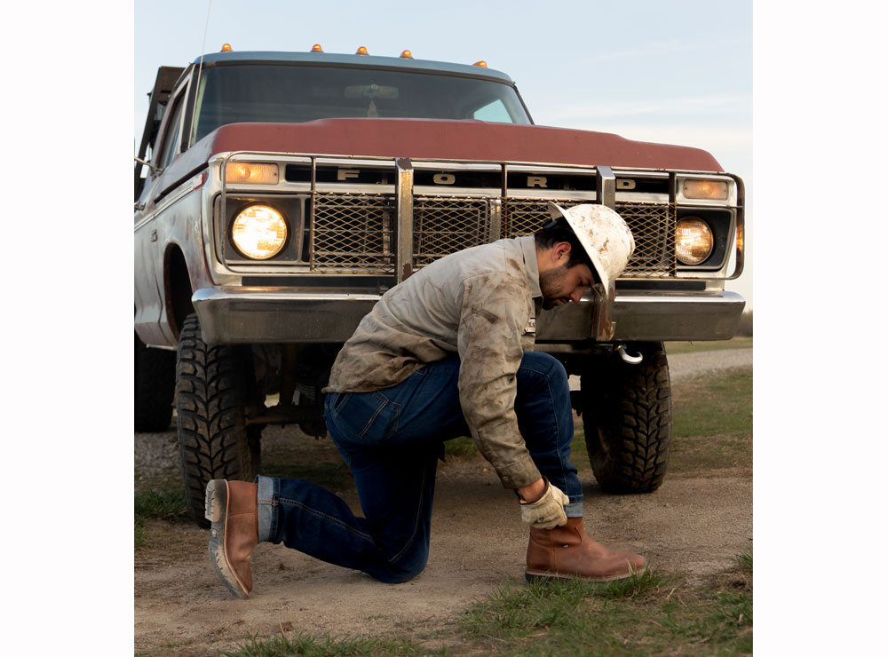 Un hombre posando delante de una vieja camioneta Ford y poniéndose las botas.